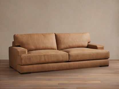Tan leather Norwalk Sofa with two backrest cushions and sleek armrests placed on a wooden floor against a neutral wall.