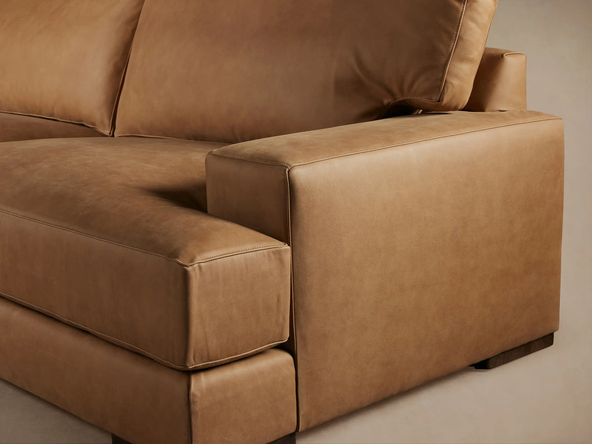 Brown leather Norwalk sofa with plush backrest and wide armrests on a wooden floor, set against a neutral background.
