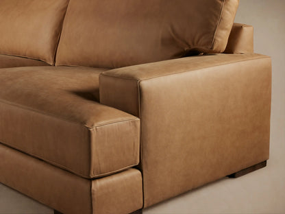 Brown leather Norwalk sofa with plush backrest and wide armrests on a wooden floor, set against a neutral background.