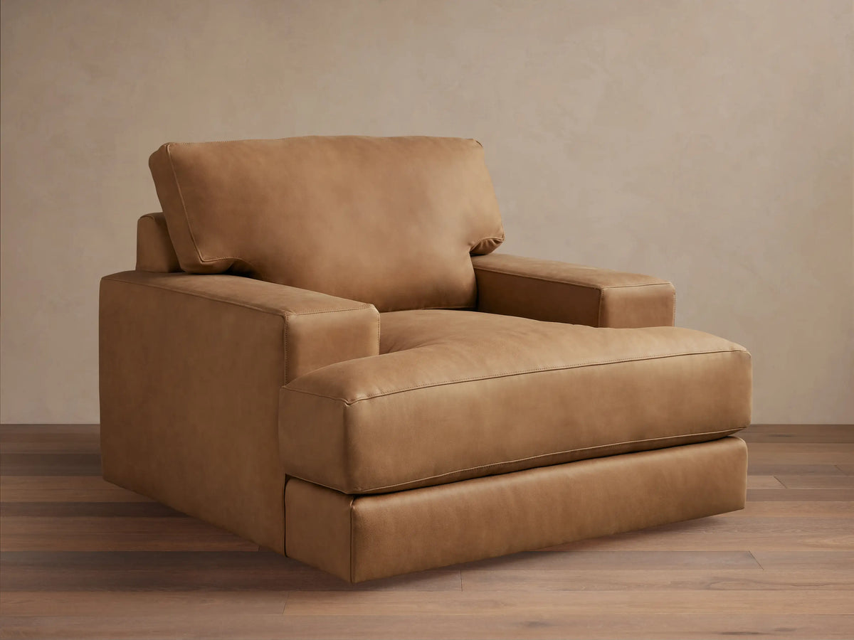 Norwalk Leather Swivel Chair in tan leather with a plush cushion, square armrests, and a broad backrest on a wooden floor.