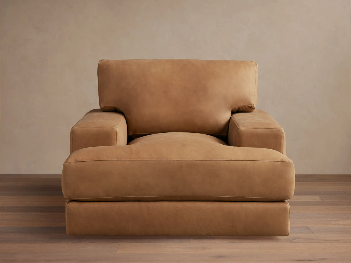 Norwalk Leather Swivel Chair in tan leather with a plush cushion, square armrests, and a broad backrest on a wooden floor.