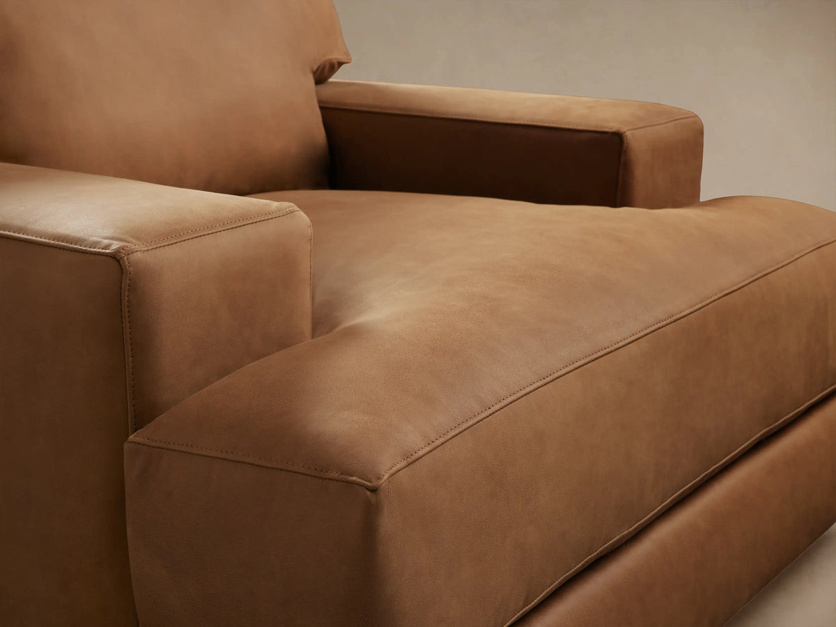 Norwalk Leather Swivel Chair in tan leather, front view. Features plush cushions, wide armrests, and a solid base on wooden floor.