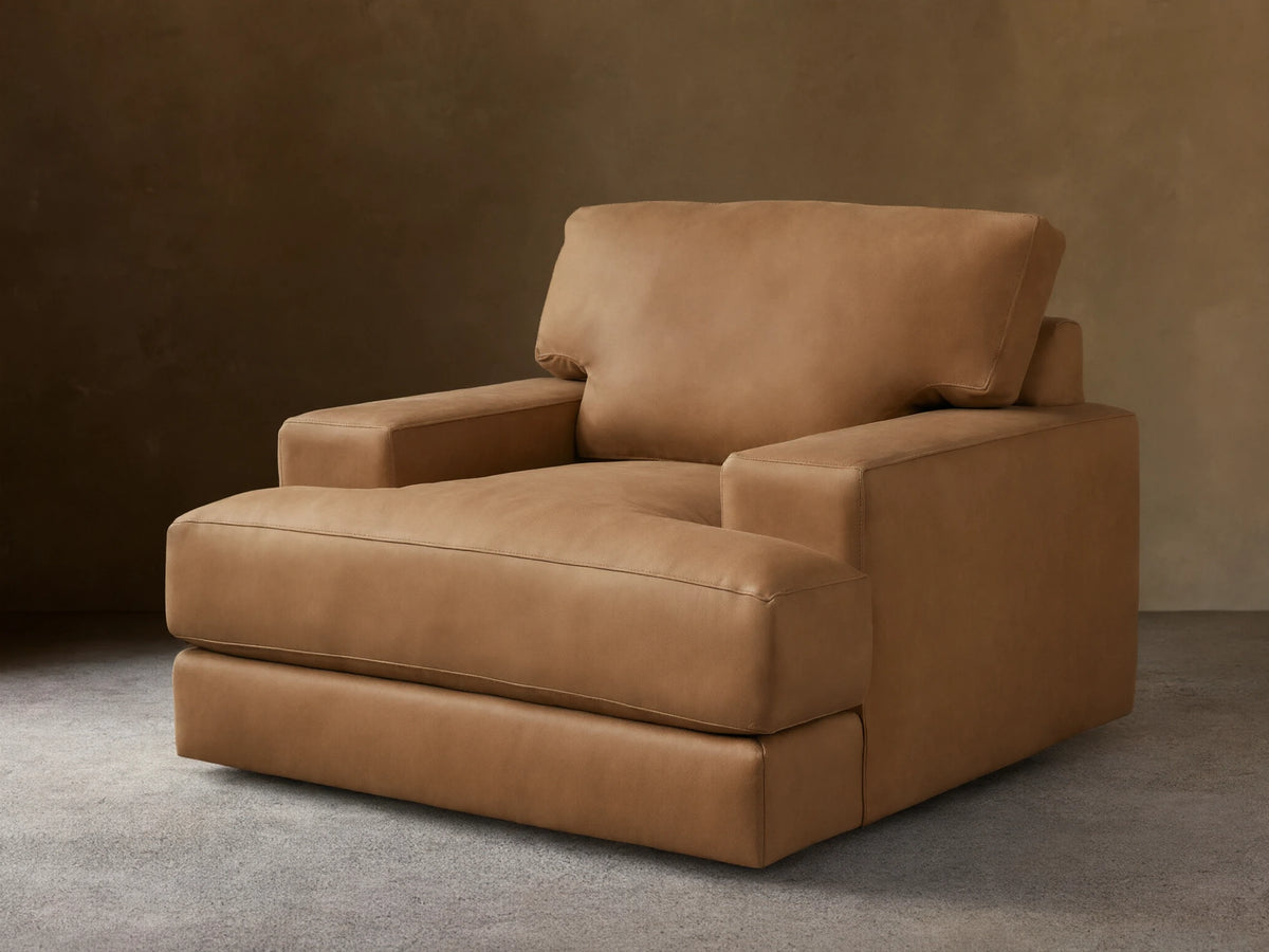 Norwalk Leather Swivel Chair in tan leather with a plush cushion, square armrests, and a broad backrest on a wooden floor.