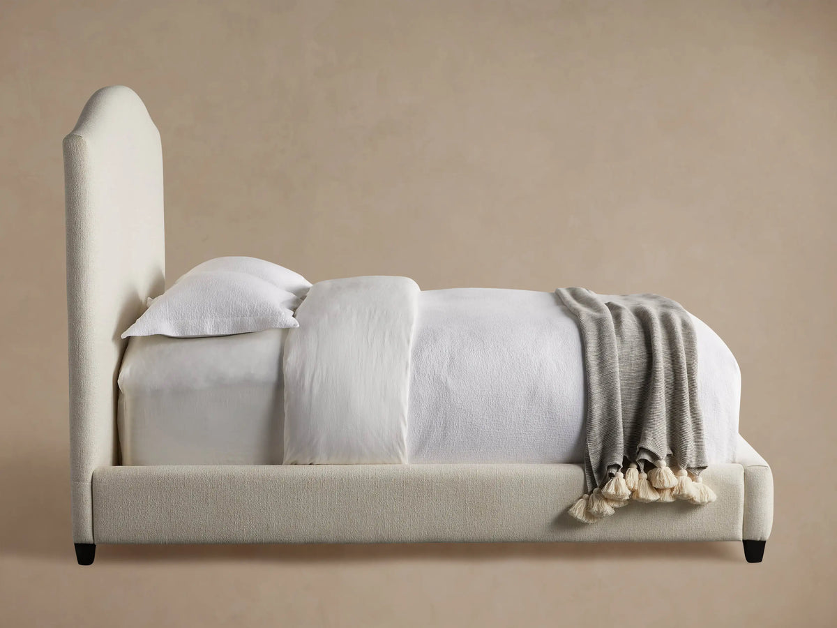 Close-up of Omani Bed's light beige, textured fabric upholstery on a softly rounded headboard corner.