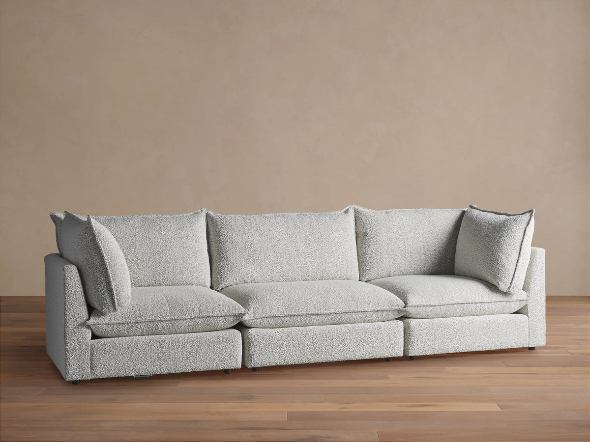 Owen Three-Piece Modular Sofa with light gray, textured bouclv©-like fabric, plump cushions & two accent pillows, against a beige wall.