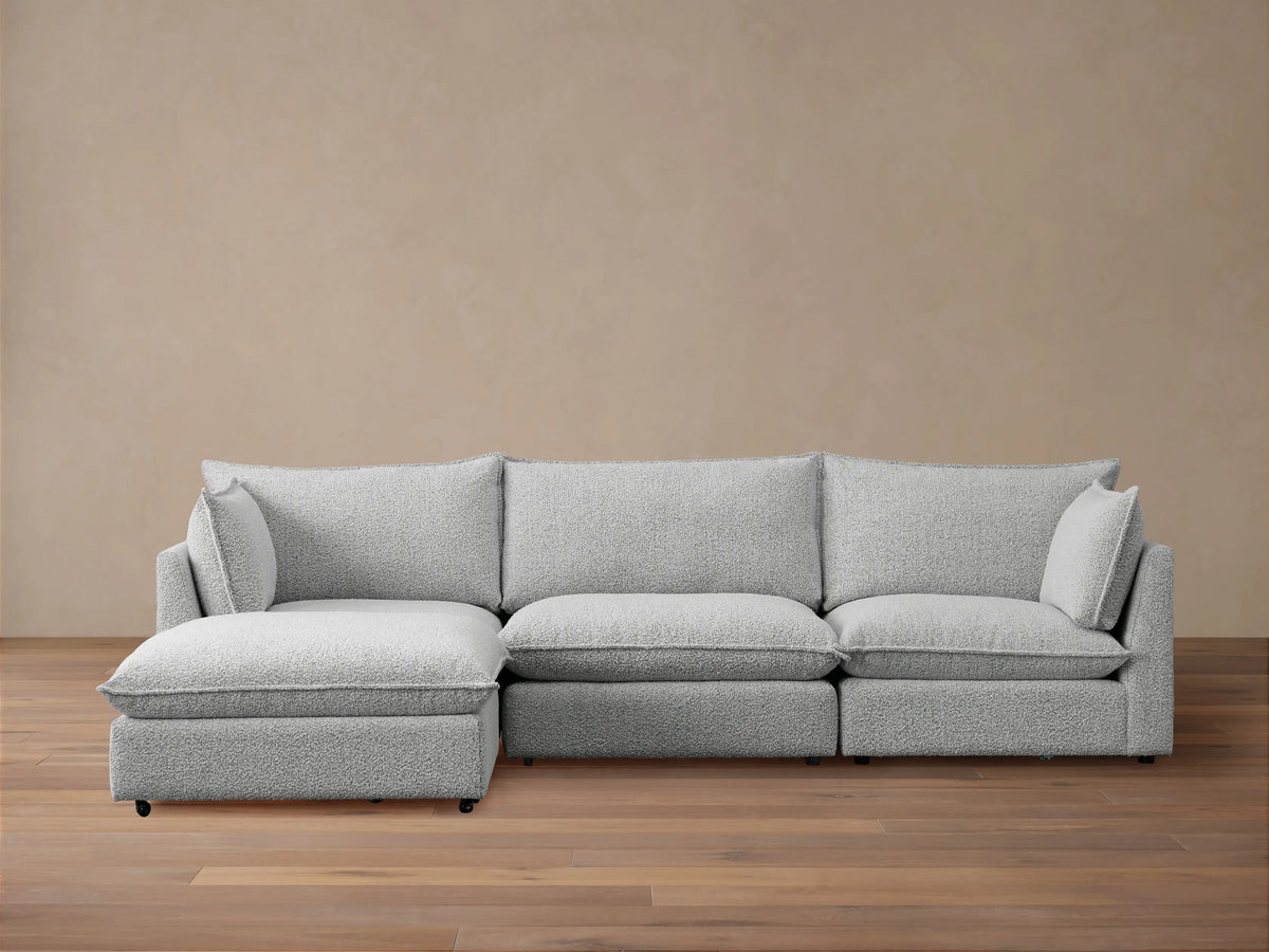 Front view of Owen Four-Piece Sectional in light grey Burbank Pepper textured fabric, chaise on left, against a beige wall, wooden floor.