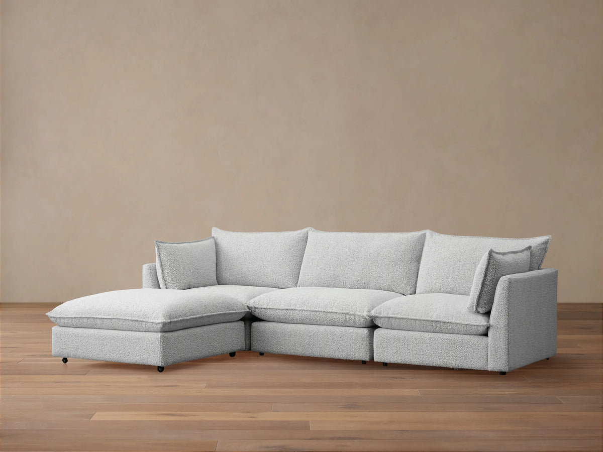 Front view of Owen Four-Piece Sectional in light grey Burbank Pepper textured fabric, chaise on left, against a beige wall, wooden floor.
