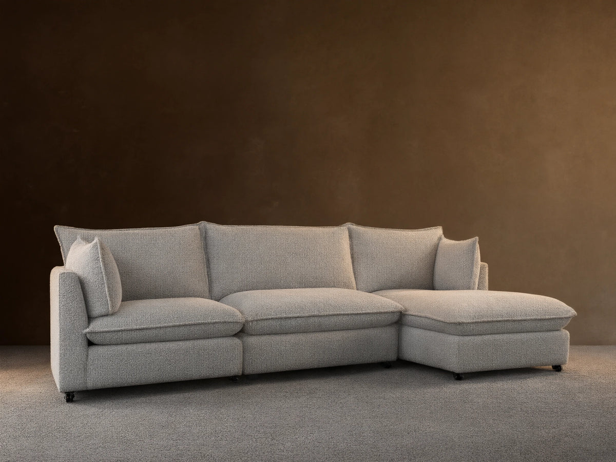 Front view of Owen Four-Piece Sectional in light grey Burbank Pepper textured fabric, chaise on left, against a beige wall, wooden floor.