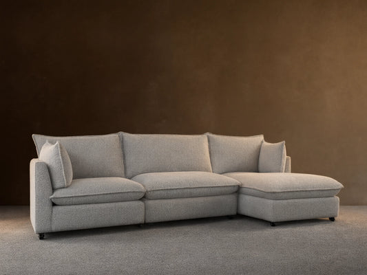 Front view of Owen Four-Piece Sectional in light grey Burbank Pepper textured fabric, chaise on left, against a beige wall, wooden floor.