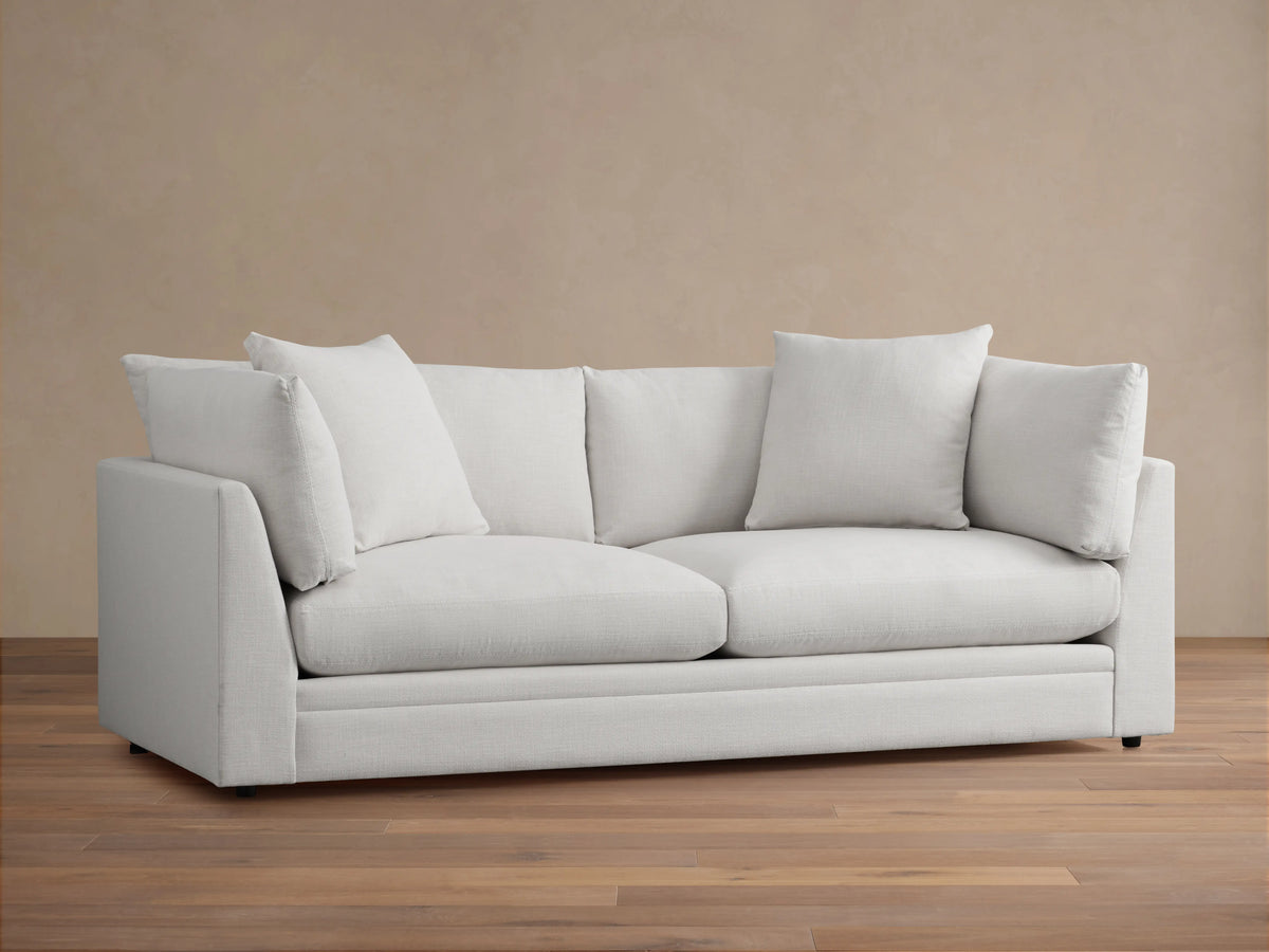 Pavo Sofa in Barbados Cream fabric, showing close-up of corner with plush seat and back cushions, smooth texture, and neutral color.