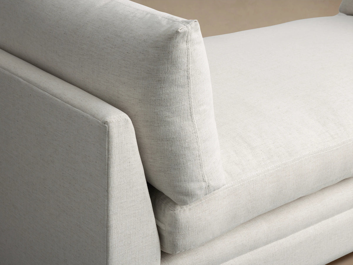 Cream-colored Pavo Daybed with plush cushions on either end, set against a neutral wall on a wooden floor.