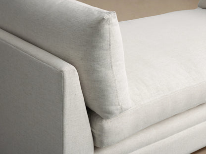 Cream-colored Pavo Daybed with plush cushions on either end, set against a neutral wall on a wooden floor.