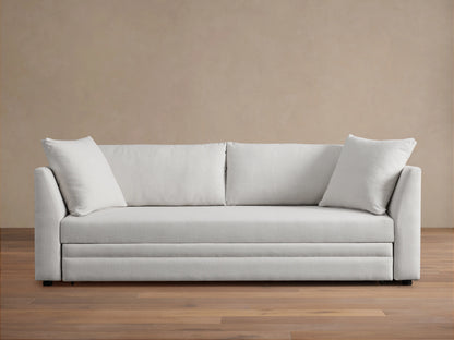 Pavo Trundle Sleeper Sofa in cream fabric, features a sleek design with straight arms and three large seat cushions. Set in a minimalist room.