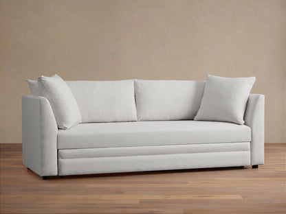 Pavo Trundle Sleeper Sofa in cream fabric, features a sleek design with straight arms and three large seat cushions. Set in a minimalist room.