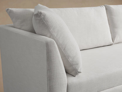 Pavo Trundle Sleeper Sofa in cream fabric with three back cushions, two side cushions, and a streamlined design on a wooden floor.