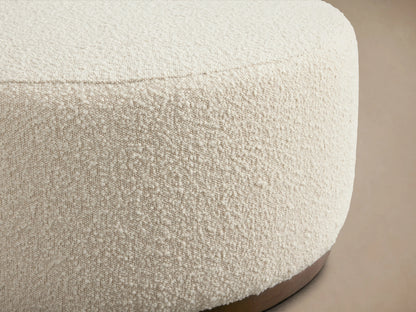 Ryles Plinth Ottoman in close-up, featuring a textured cream fabric and smooth wooden base. Edges are slightly rounded.
