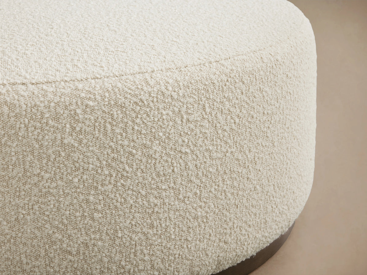 Ryles Plinth Ottoman with textured cream fabric, close-up showing rounded edge and subtle weave on a wooden base.
