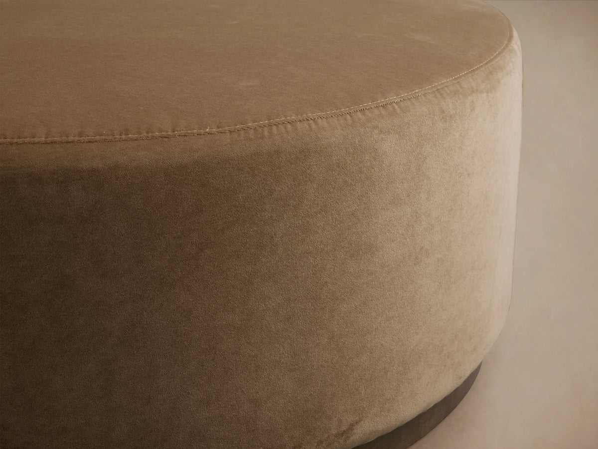 Ryles Plinth Ottoman in beige fabric, close-up view showcasing its round shape and smooth upholstery with visible stitching.