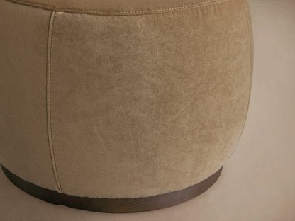 Ryles Plinth Ottoman in beige fabric, close-up of rounded side showing textured surface and dark wooden base on light backdrop.