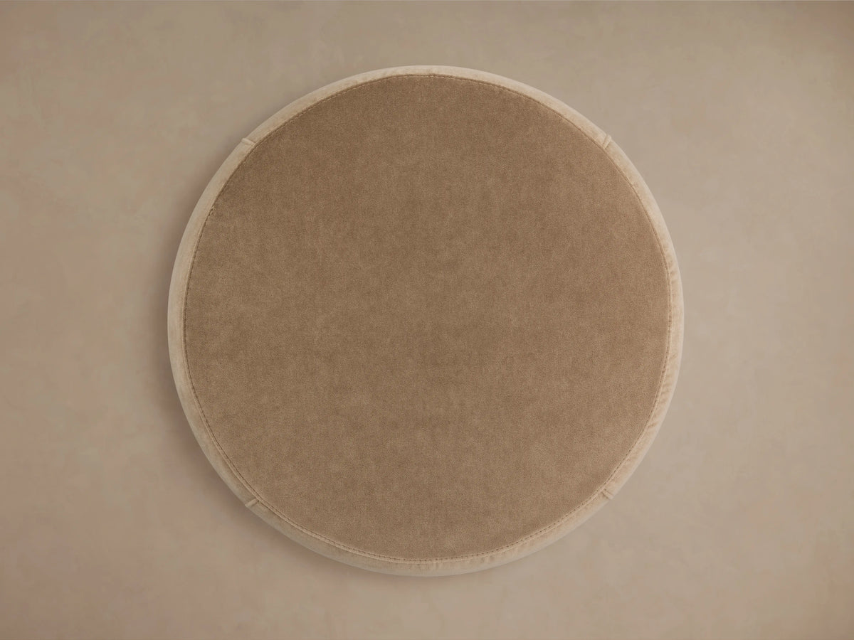 Round Ryles Plinth Ottoman in beige fabric, top view. The ottoman has a smooth surface with a subtle texture and light-colored edge trim.