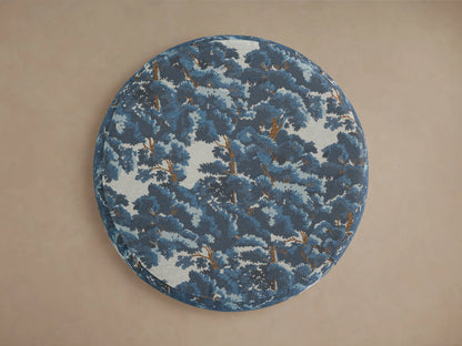 Ryles Plinth Ottoman in Oaks Pacific fabric with blue and white tree pattern, round shape, and wooden base on a beige background.