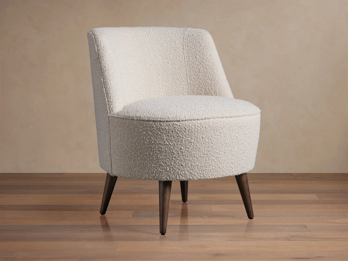 Ryles Chair, off-white boucle accent chair angled right, with curved back and dark tapered legs on wood floor.