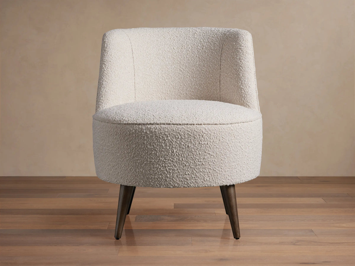 Ryles Chair, off-white boucle accent chair angled right, with curved back and dark tapered legs on wood floor.