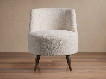 Ryles Chair, off-white boucle accent chair angled right, with curved back and dark tapered legs on wood floor.