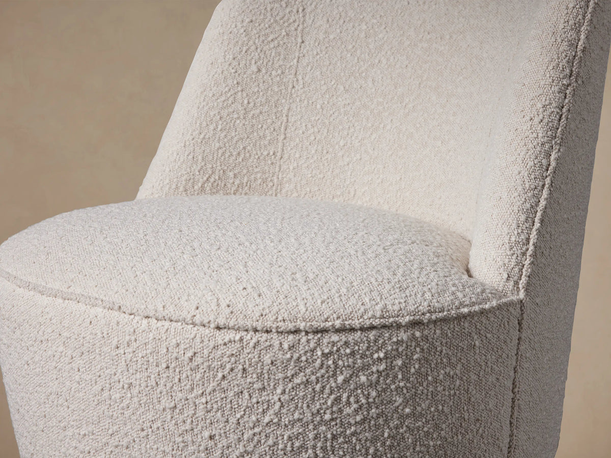 Front view of the Ryles Chair, an armless cream bouclv© upholstered chair with a curved back and dark tapered wood legs, on a wood floor.