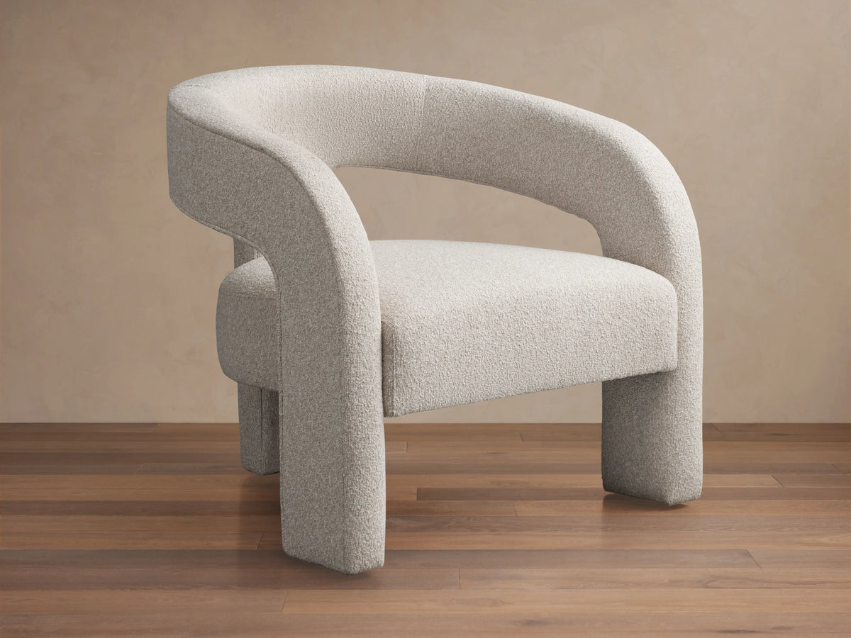 Light grey Mara Cutout Chair with textured fabric, modern curved arms and stout legs, angled on a wood floor.