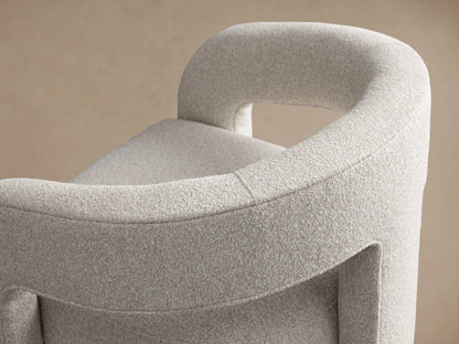 Light grey Mara Cutout Chair with textured fabric, modern curved arms and stout legs, angled on a wood floor.