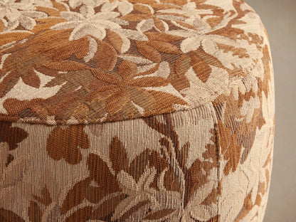 Close-up of the Ryles Ottoman's brown, tan, and cream woven floral pattern fabric, showing the curved side.