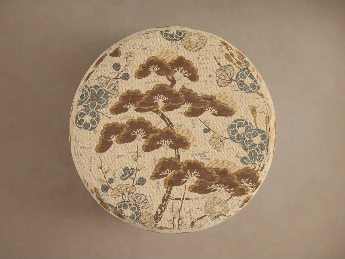 Close-up of Ryles Ottoman upholstered in textured cream fabric with a brown, light blue, and gold botanical pattern.