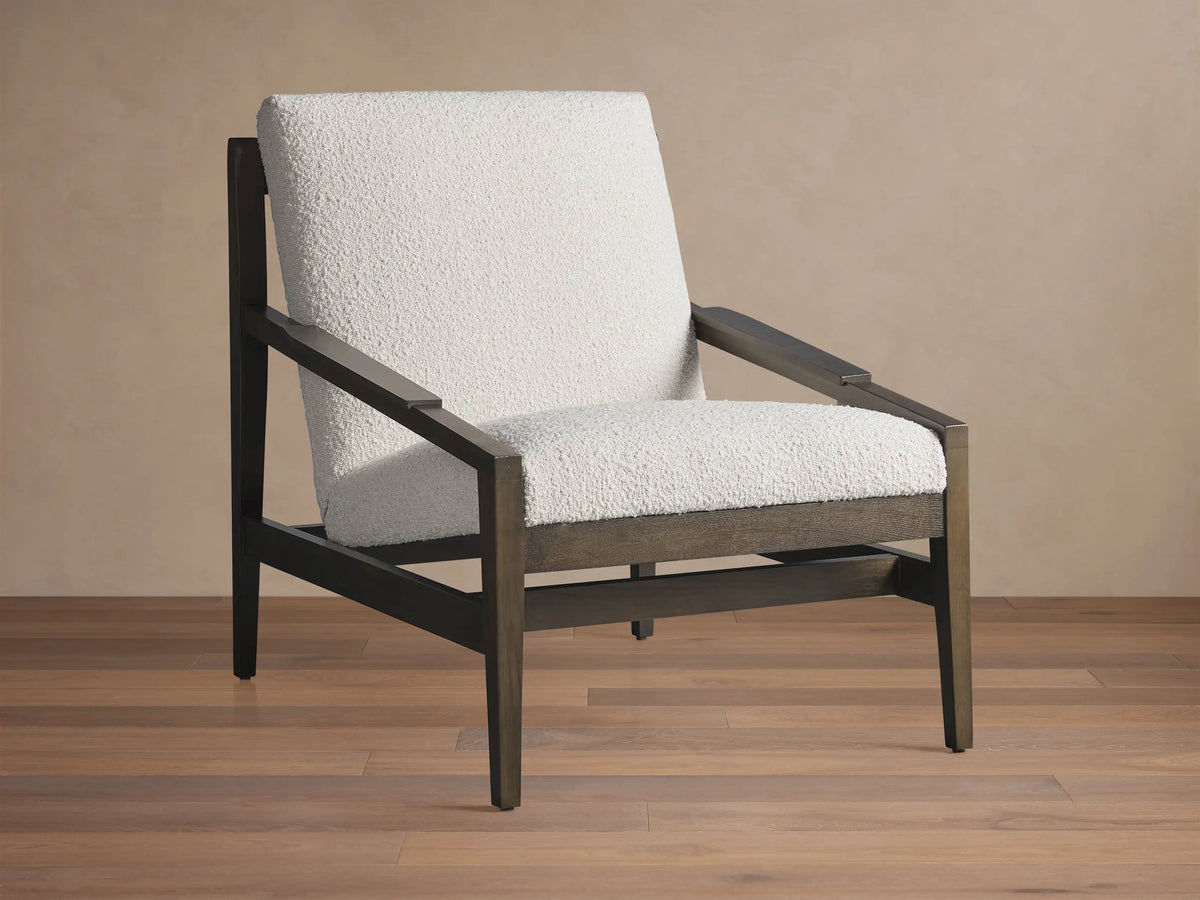 Sarlow Chair, modern design, dark wood frame, and textured off-white upholstery, on a wooden floor against a beige wall.