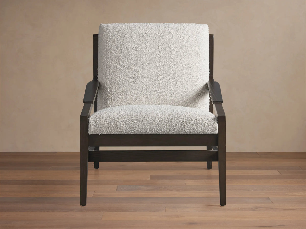 Sarlow Chair, modern design, dark wood frame, and textured off-white upholstery, on a wooden floor against a beige wall.