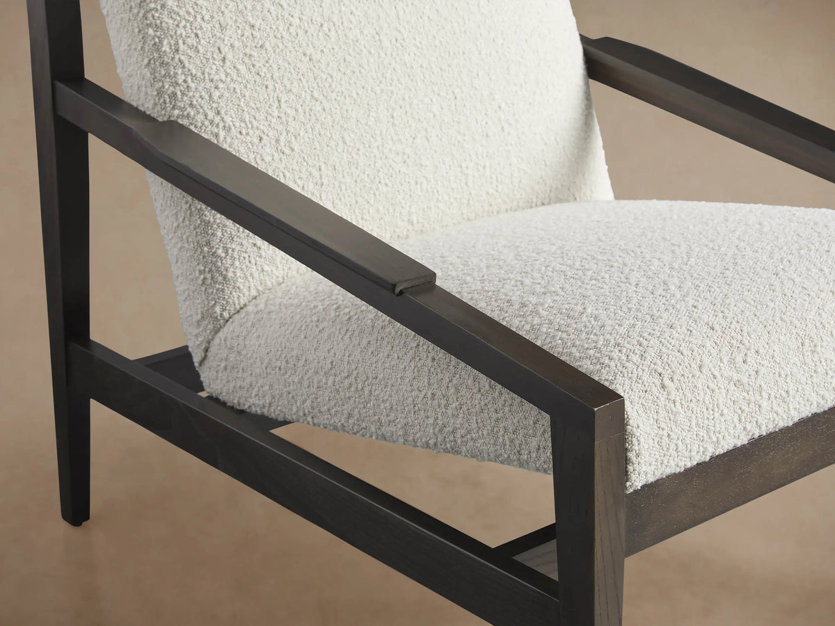 Sarlow Chair, front view. Dark brown wooden frame with creamy white textured upholstery, on a wood floor against a light wall.