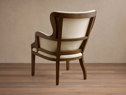 Rear view of the Tilly Chair, showing its dark wood frame, light beige woven upholstery, and brass nailhead detailing.