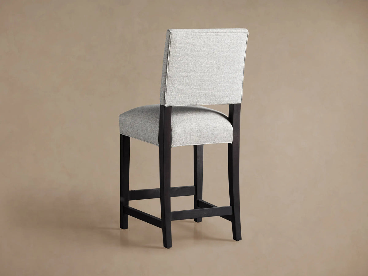 Torino Stool's upholstered backrest, textured off-white fabric, with a glimpse of the dark wooden frame. Angled view.