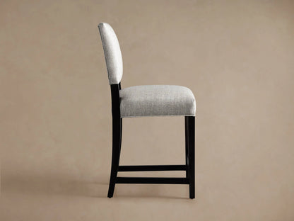 Torino Stool, back view. Light grey upholstered seat and backrest, dark wood tapered & splayed legs, on beige background.