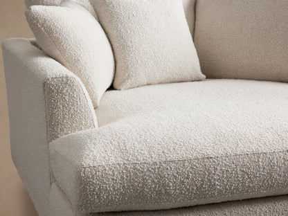 Light cream Vernon Two-Piece Cuddle Chaise Sectional with textured fabric and pillows, L-shaped, on wood floor against a tan wall.