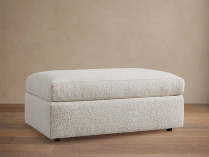 Light cream textured Vernon Ottoman, rectangular, with a soft top cushion, centered on a wooden floor.