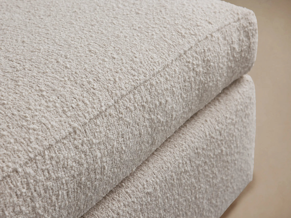 Vernon Ottoman, rectangular, upholstered in plush, off-white textured fabric, sitting on a wooden floor against a light wall.