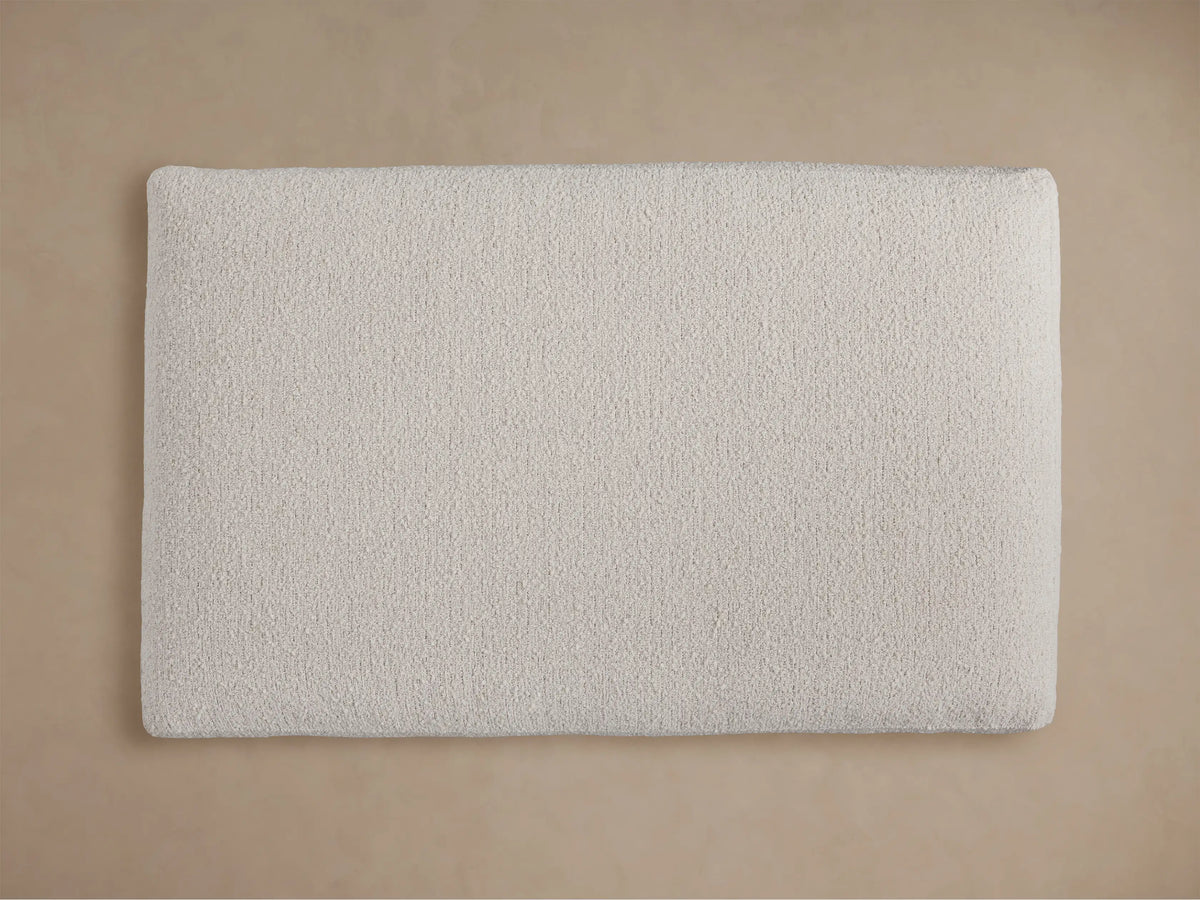 Angled close-up of Vernon Ottoman, showcasing its light cream, textured, nubby bouclv© fabric surface.