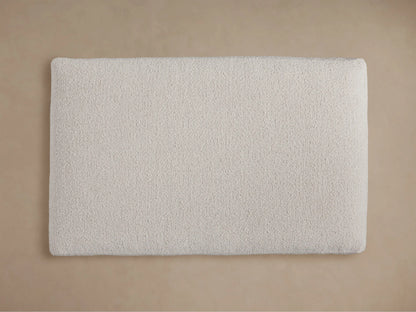 Angled close-up of Vernon Ottoman, showcasing its light cream, textured, nubby bouclv© fabric surface.
