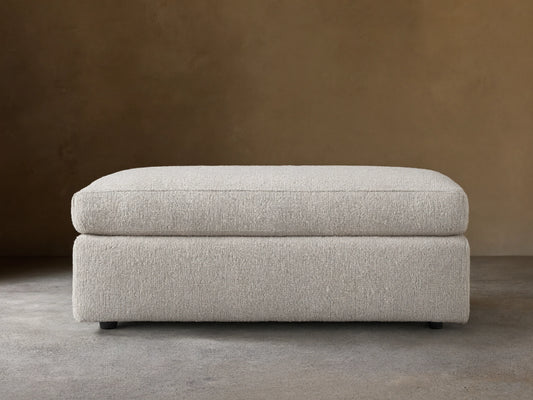 Light cream textured Vernon Ottoman, rectangular, with a soft top cushion, centered on a wooden floor.