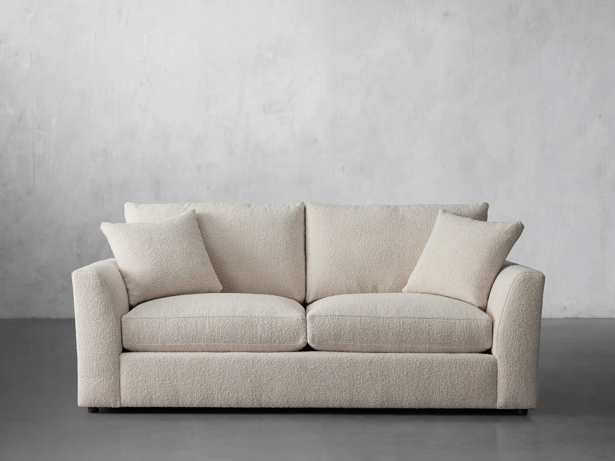 Front view of a Vernon Sofa, a cream bouclv© two-seater couch, featuring two back cushions and two matching throw pillows.