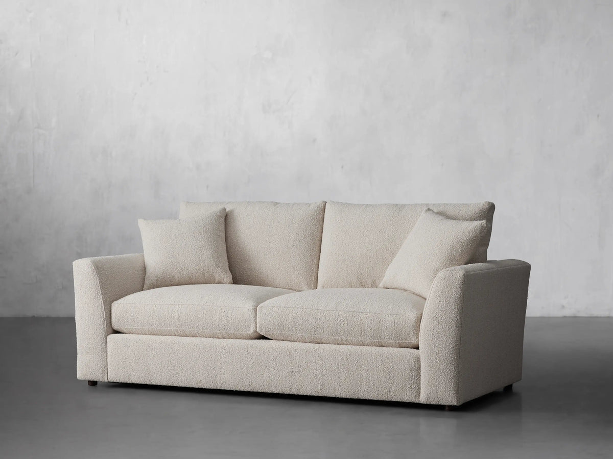Front view of a Vernon Sofa, a cream bouclv© two-seater couch, featuring two back cushions and two matching throw pillows.