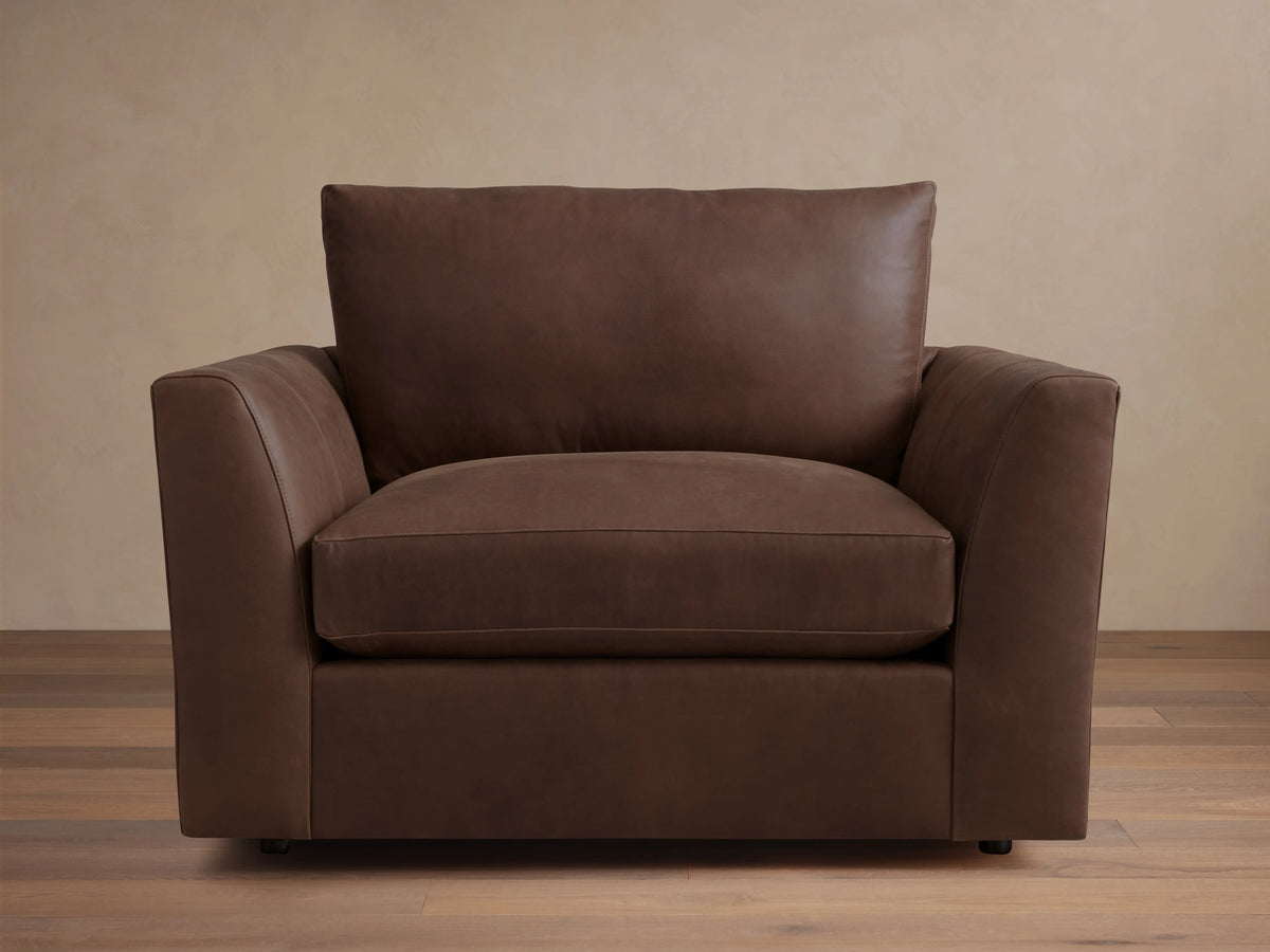 Vernon Leather Chair in dark brown leather, featuring a boxy silhouette with plush cushions and straight armrests, set against a wood floor.