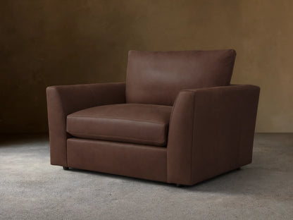 Vernon Leather Chair in dark brown leather, featuring a boxy silhouette with plush cushions and straight armrests, set against a wood floor.