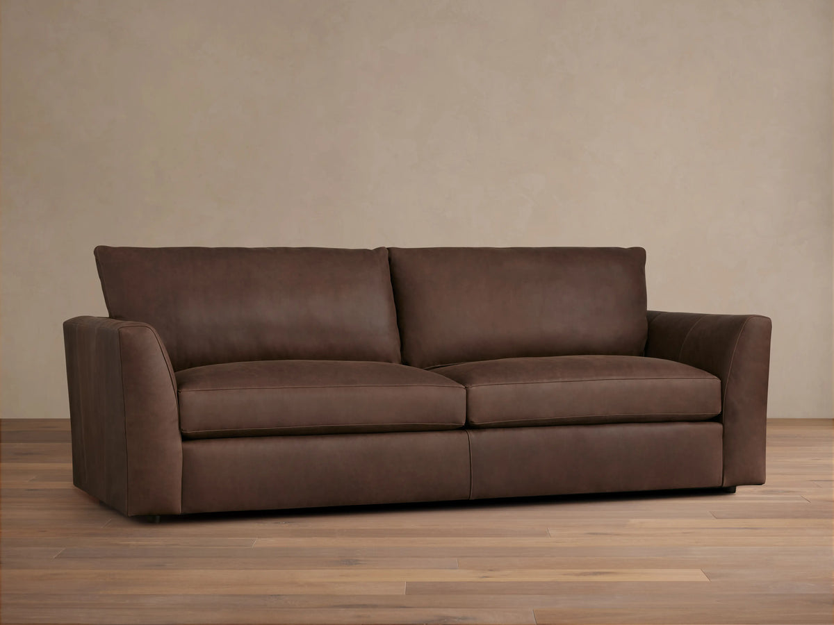 Vernon Leather Sofa featuring a rich brown finish, plush seat cushions, wide armrests, and clean lines, set against a neutral wall.